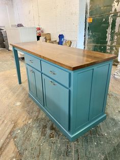 a blue kitchen island with wooden top in an unfinished room