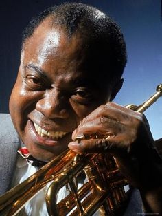 a man holding a trumpet in his right hand and smiling at the camera while wearing a suit