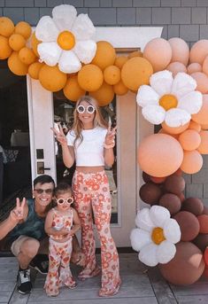 a woman and two children standing in front of a balloon arch with flowers on it