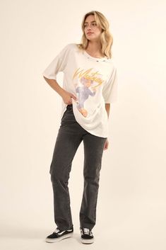 a woman standing in front of a white wall wearing jeans and a t - shirt