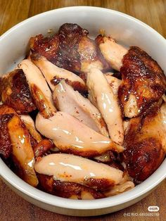 a white bowl filled with sliced chicken on top of a wooden table