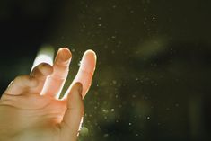 a person holding their hand up in the air with water droplets all around them on a dark background