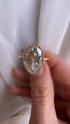 a close up of a person holding a ring with an oval shaped diamond in it