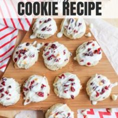 a wooden cutting board topped with cookies covered in white frosting and cranberry toppings