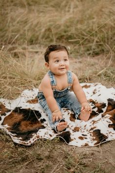 a baby sitting on top of a cow print blanket