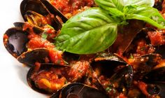 a white plate topped with mussels covered in tomato sauce and garnished with basil