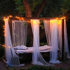 a canopy bed with lights on it in the middle of a garden at night time