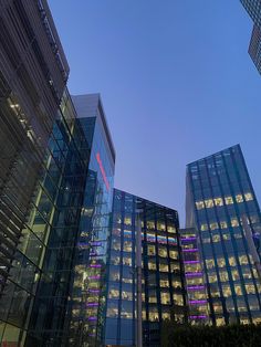 some very tall glass buildings with lights on at night time in front of blue sky