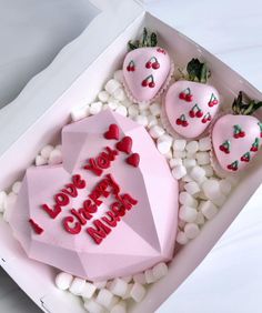 a pink heart shaped cake in a box surrounded by white rocks and marshmallows