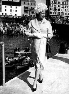 an old photo of a woman walking on the dock with people in boats behind her