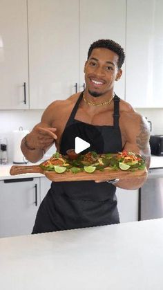 a man holding a pizza on top of a wooden cutting board in a white kitchen