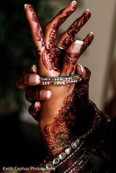 a woman's hands with henna tattoos and bracelets on her wrist, holding up two fingers