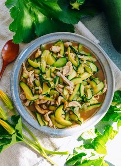 a bowl filled with zucchini and mushrooms next to green vegetables on a towel