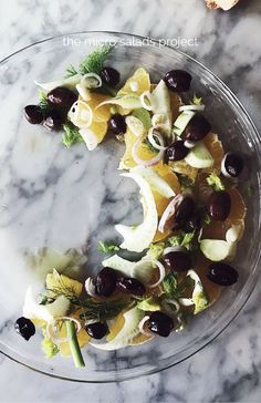 a glass bowl filled with lots of food on top of a marble countertop next to a knife and fork