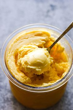 a glass bowl filled with ice cream on top of a gray counter next to a wooden spoon