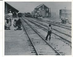 an old black and white photo of people standing on train tracks in the middle of town