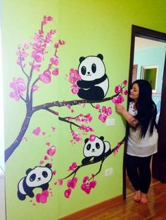 a woman standing in front of a wall painted with pandas and cherry blossom trees