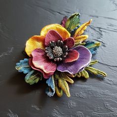 a colorful flower brooch sitting on top of a black table next to a wall