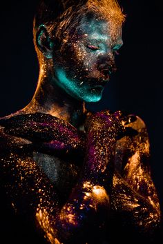 a woman is covered in gold and blue powder with her hands on her chest,