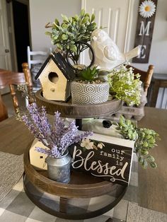 three tiered tray with flowers and birdhouse decorations on the top, sitting on a dining room table