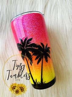 a pink and yellow tumbler with palm trees on it sitting on a white fur