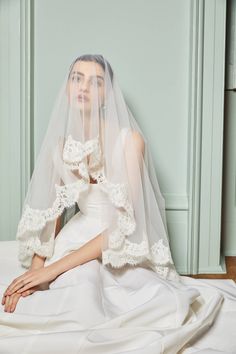 a woman in a white wedding dress sitting on a bed with a veil over her head