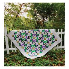 a quilted table runner with purple, green and yellow flowers on it in front of a white fence