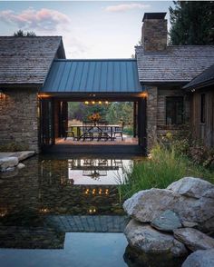 an outdoor dining area is lit up by lights and surrounded by large rocks, with a pond in the foreground