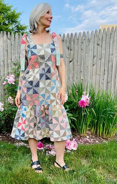 an older woman standing in front of a fence wearing a dress made out of squares