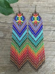 two pairs of multicolored beaded earrings on top of a wooden table next to a green leaf