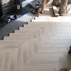 two men working on herringbone flooring in a room with an open fire place