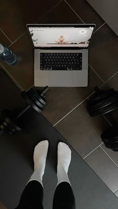 a person standing in front of a laptop computer on top of a floor next to a pair of black dumbbells