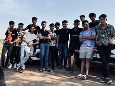 a group of young men standing next to a white car in the middle of a dirt road