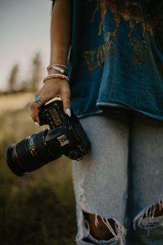 a person holding a camera in their hand with grass and trees in the back ground