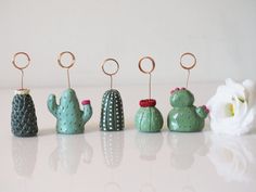 small cactus figurines are lined up in a row on a white surface, with rings hanging from them