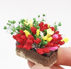 a miniature piece of wood with flowers on it in someone's hand and white background