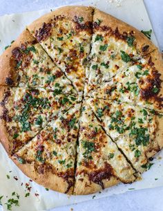 a pizza with cheese and herbs cut into slices on a piece of white parchment paper