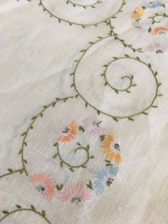 an embroidered tablecloth with flowers and vines on the edges, in pastel colors