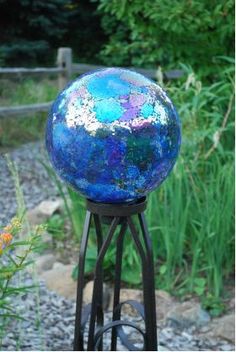 a blue ball sitting on top of a metal stand next to some grass and flowers