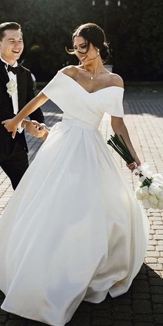 a bride and groom are walking down the street in their wedding attire, holding hands