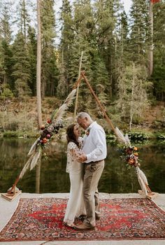 a man and woman standing next to each other on top of a rug in front of a lake