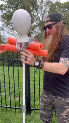 a man with long hair and beard standing next to a fence holding an orange object