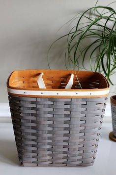 a gray basket with two white handles next to a potted plant