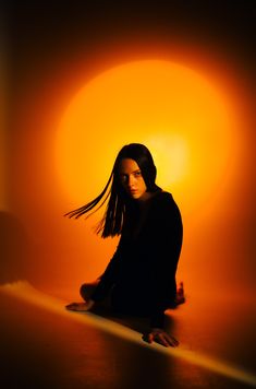 a woman is sitting on the floor in front of an orange light with long hair