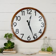 a clock on the wall next to some books and succulents in a vase