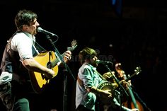 two men are playing guitars and singing into microphones in front of an audience at a concert