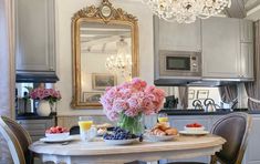 a dining room table with flowers and fruit on it in front of a large mirror