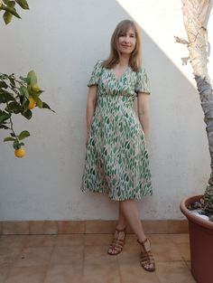 a woman standing in front of a tree wearing sandals and a green dress with leaves on it