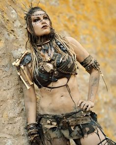 a woman with tattoos and chains on her body is standing next to a rock wall