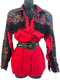 Add a touch of vintage style to your wardrobe with this black and red Adobe Rose western rodeo fringe cowgirl blouse. The blouse features a collared neckline, button closure, and long classic/fitted sleeves. The fringe accents and floral pattern add a unique touch to the blouse, making it perfect for any party or cocktail occasion. Made of 100% cotton, this blouse is machine washable and comes in a size M. The blouse is an authentic original vintage style, with a classic fit and size type. It is Western Style Blouse For Spring Rodeo, Fall Rodeo Long Sleeve Blouse, Fall Long Sleeve Blouse For Rodeo, Black Top For Spring Rodeo, Spring Long Sleeve Blouse For Rodeo, Red Western Long Sleeve Tops, Western Style Red Long Sleeve Tops, Red Long Sleeve Western Top, Fitted Western Blouse For Fall